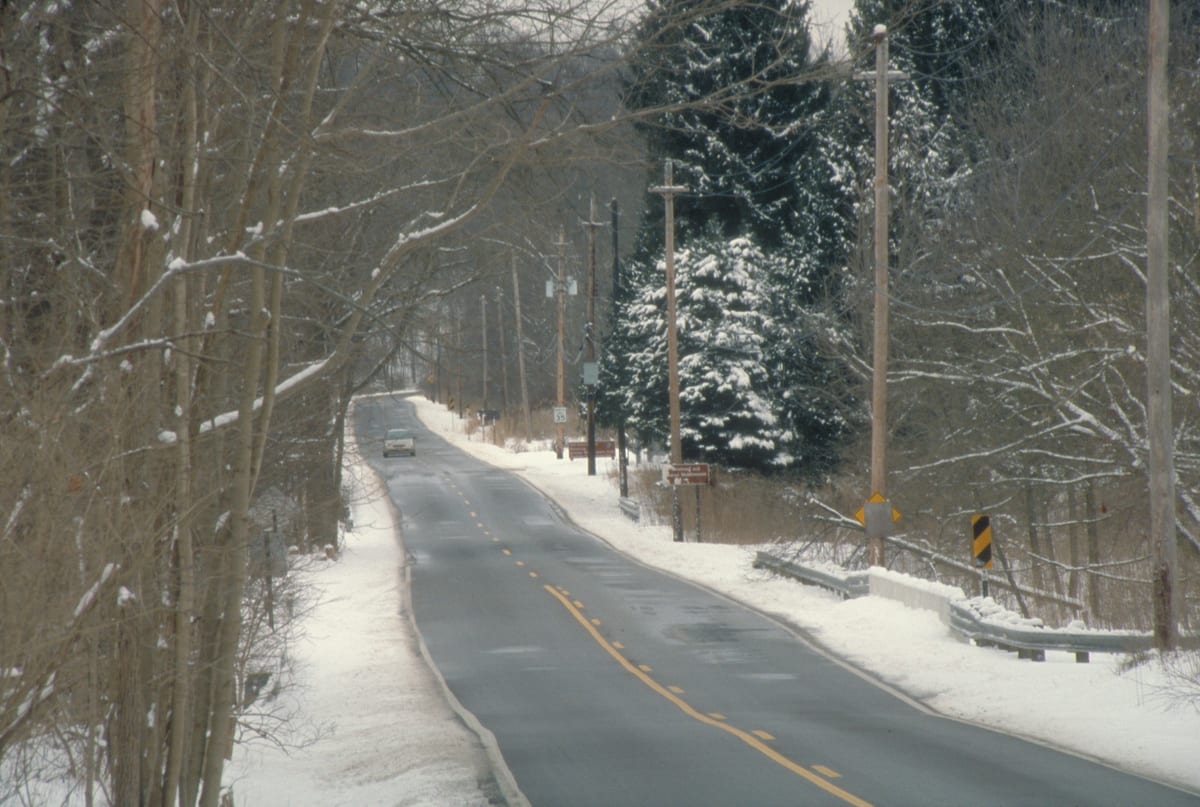 Car driving on a quiet road through snowy trees near the Ohio and Erie Canalway